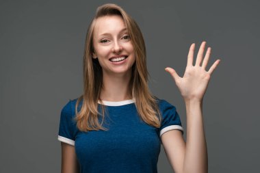 Çekici, sosyal, güler yüzlü, sarışın, düz saçlı, el sallayan bir kız. Merhaba de, merhaba. seni selamlıyorum, misafirleri selamlıyorum. İnsani duygular, yüz ifadesi kavramı.