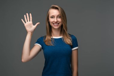 Çekici, sosyal, güler yüzlü, sarışın, düz saçlı, el sallayan bir kız. Merhaba de, merhaba. seni selamlıyorum, misafirleri selamlıyorum. İnsani duygular, yüz ifadesi kavramı.