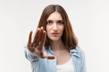 Uzun kestane rengi saçları olan ciddi bir kız, gündelik kıyafetlerle giyinmiş, eli ile durduğunu gösteriyor, reddedildiğini gösteriyor, şiddete, vücut diline izin vermiyor. İnsani duygular, yüz ifadesi kavramı.