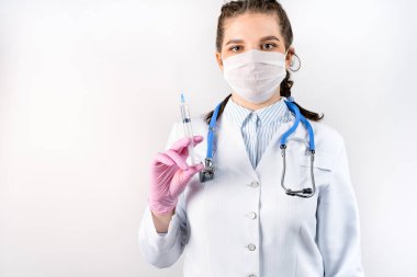 Beyaz önlüklü, tıbbi maskeli ve pembe steril eldivenli genç bayan doktor elinde şırınga tutuyor. Aşı konsepti. Tıbbi konsept.