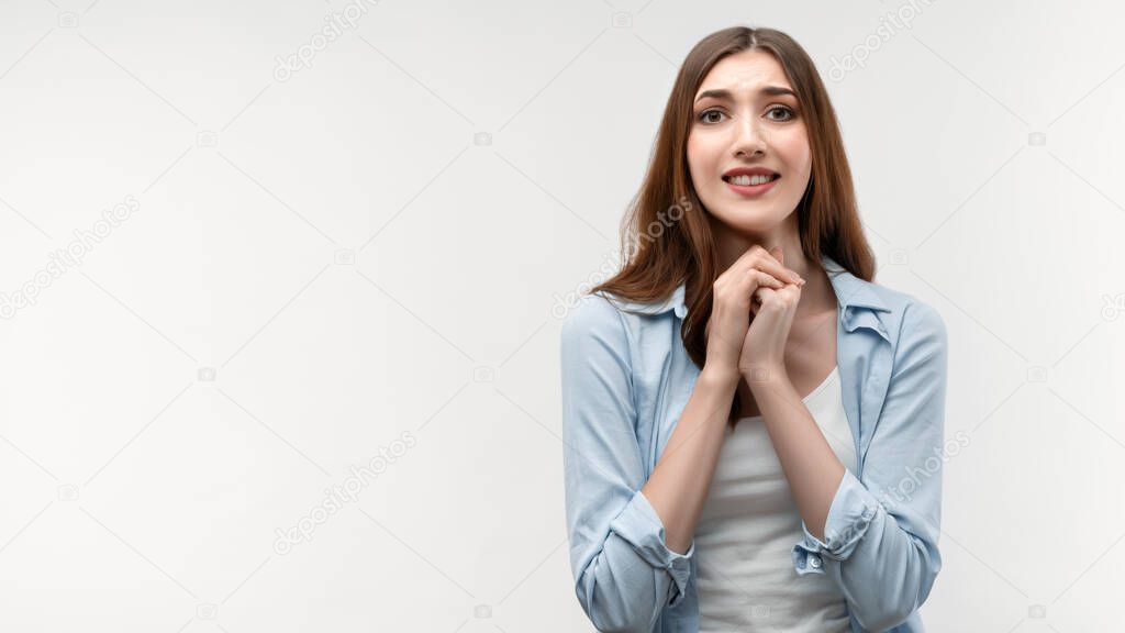 Photo of charismatic brunette female with long straight hair, dressed in casual clothes, keeps hands together near chin, smiles gently, has cute expression. Human emotions, facial expression concept.