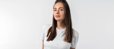 Uzun kestane rengi saçları olan, beyaz duvar arkasına izole edilmiş gibi poz veren tasasız, modern genç bir kız. Halk yaşam tarzı konsepti.
