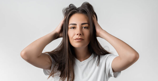 Довольно беззаботная современная девушка с длинными каштановыми волосами, прижатыми к голове или трогательными волосами. Изолированный на белом фоне. Выражения, выражения, прическа и концепция людей.