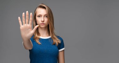 Mavi tişörtlü, sarı düz saçlı, ciddi bir kız eli ile durduğunu gösteriyor, işaret ediyor, reddedildiğini gösteriyor, şiddete, vücut diline izin vermiyor. Metnin için boşluk kopyala