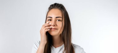 Uzun kestane rengi saçları olan, beyaz duvar arkasına izole edilmiş gibi poz veren tasasız, modern genç bir kız. Halk yaşam tarzı konsepti.