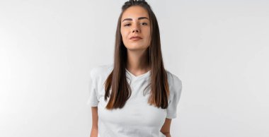 Uzun kestane rengi saçları olan, beyaz duvar arkasına izole edilmiş gibi poz veren tasasız, modern genç bir kız. Halk yaşam tarzı konsepti.