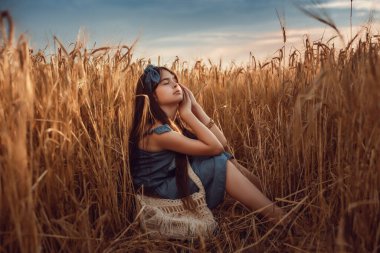 10-12 yaşlarında, uzun kahverengi saçlı bir kızın portresi. Bir yaz akşamında buğday tarlasında yürüyor. Seçici odak, ton ve gürültüye sahip resim