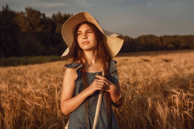 10-12 yaşlarında, uzun kahverengi saçlı bir kızın portresi. Bir yaz akşamında buğday tarlasında yürüyor. Seçici odak, ton ve gürültüye sahip resim