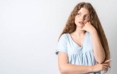 Dalgın Avrupalı, uzun kıvırcık saçlı genç bir kadının fotoğrafı. Düşünceli bir ifadeyle yukarı bakıyor. Beyaz arka planda izole edilmiş. Metnin için boşluk kopyala