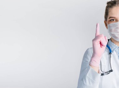 Beyaz önlüklü ve pembe steril eldivenli güzel kadın doktor, beyaz arka planda parmak izi olan bir işaret gösteriyor..