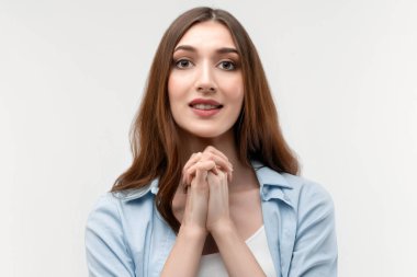 Karizmatik esmer kadın fotoğrafı, uzun düz saçlı, günlük kıyafetler giymiş, çenesinin yanında el ele tutuşan, nazikçe gülümseyen, hoş bir yüz ifadesi olan. İnsani duygular, yüz ifadesi kavramı.