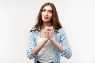 Uzun kestane rengi saçları olan, günlük kıyafetler giymiş, izole beyaz arka planda kalp sembolü yapan güzel bir genç kadın. Romantik konsept.