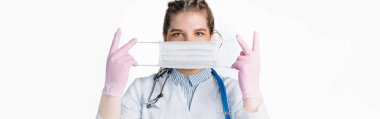 Beyaz önlüklü ve pembe steril eldivenli genç bayan doktor beyaz arka plana beyaz koruma maskesi takıyor. Tıbbi konsept
