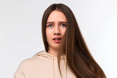 Uzun kestane rengi saçlı, şık bej kapüşonlu bir kadın. Şüphe, belirsizlik ve karmaşa kavramı