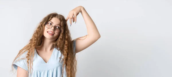 Photo of Pensive girl with curly long hair, and in round spectacles, looking up having pensive expression and holding her hand near head. Isolated over white background. Copy space for your text