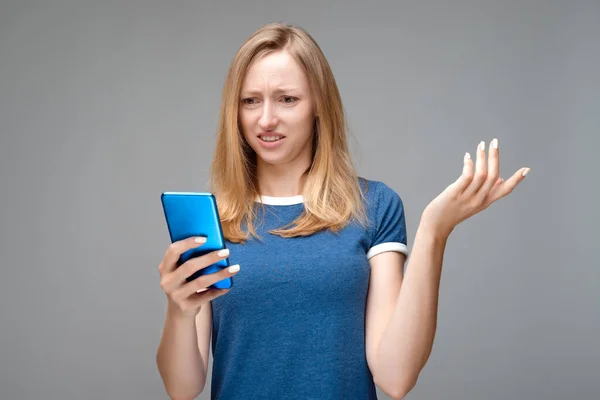Sarı saçlı ve mavi tişörtlü rahatsız bir kız sorunlu bir yüz ifadesi var, akıllı telefon tutuyor, avuç içi kaldırıyor, sorunun ne olduğunu anlayamıyor, mesajın garip bir anlamı var, omuzlarını silkiyor.