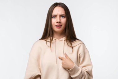 Uzun düz saçlı, öfkeli esmer bir kadının fotoğrafı, kendini parmağıyla gösteriyor, ağzı açık, şaşırıyor, hoşnutsuz bir ifade sergiliyor, kırıcı sözlerle ürküyor..