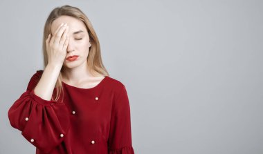 Uzun sarı saçlı yorgun Avrupalı genç bir kadının fotoğrafı, yüzünü kapatıyor, gözlerini kapatıyor, yorgunluk hissediyor, dinlenmeye ihtiyacı var, uykulu bir ifadeye sahip, gri arkaplan üzerinde izole edilmiş. Metnin için boşluk kopyala