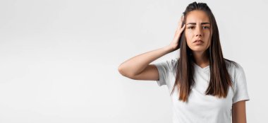 Şok olmuş, uzun kestane rengi saçları olan, günlük kıyafetlerle giyinmiş, bir kulağını beyaz arka planda tutan genç bir kadın. Sessizlik kavramını koru. Metnin için boşluk kopyala