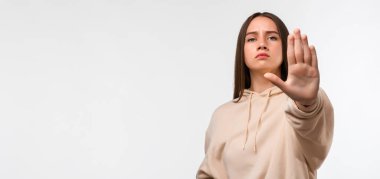 Uzun kestane rengi saçları olan, ciddi ve sert görünen, sıradan bej kapüşonlu giyinen, avuçlarını açık bırakan genç, güzel bir kadın. Metnin için boşluk kopyala