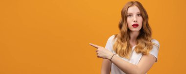 Dalgalı kızıl saçlı, beyaz tişörtlü, şaşırmış ve işaret eden güzel bir kız. Bilgin olsun diye söylüyorum. Sarı arkaplanda izole edilmiş