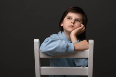 10-12 yaşlarındaki mutlu çocuk portresi, günlük kıyafetler giymiş, bir sandalyeye oturmuş ve bir şeyler hayal ediyor. İnsani duygular, yüz ifadesi kavramı