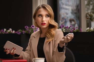 Uzun sarı saçlı, çekici bir kadın elinde telefonla bir kafede otururken erkek arkadaşını aramak istiyor.