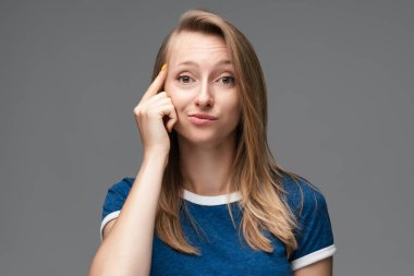 Stüdyoda kendine güvenen, düz sarı saçlı, mavi tişörtlü, başını işaret eden genç bir kadın var. Düşünce anlayışı. Akıllı ol ve düşün..