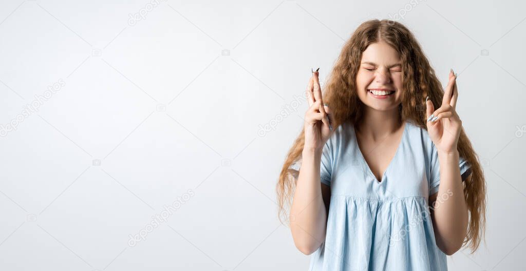 I have to win. Joyful European young woman with curly long hair raises fingers crossed, makes desirable wish, wears casual clothes, waits for good news. Copy space for your text