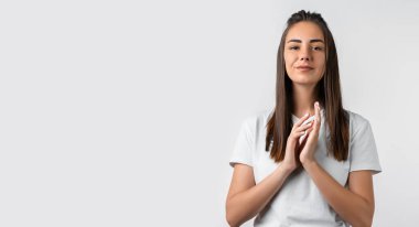 Karizmatik Avrupalı, uzun kestane rengi saçlı, el ele tutuşan hoş bir ifade takınan, beyaz tişört giyen genç bir kadının fotoğrafı. Metnin için boşluk kopyala