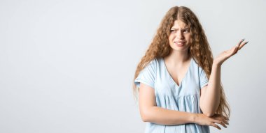 What the hell are you talking about, nonsense. Studio shot of frustrated female with curly long hairstyle gesturing with raised palm, frowning, being displeased and confused with dumb question.