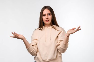 Uzun kestane rengi saçları olan, bej kapüşonlu şık giyinen, şüpheyle el ele tutuşan güvensiz genç bir kadının stüdyo fotoğrafı. Şüphe, belirsizlik ve karmaşa kavramı