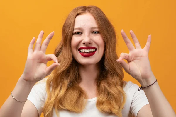 Happy girl with long wavy redhead, wearing white t-shirt Smiling and showing OK a two-handed gesture. I like that. Good job. Everything is great