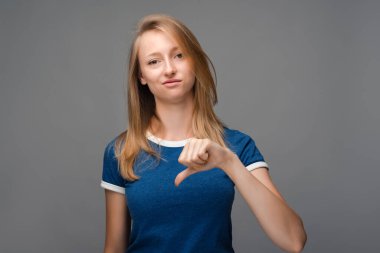 Sarışın, düz saçlı, güzel bir bayan kameraya bakıyor ve baş parmağını aşağıda tutuyor. Hoşlanmama kavramı. İnsani duygular, yüz ifadesi kavramı