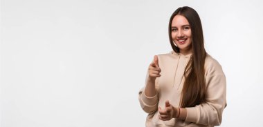 Uzun kestane rengi saçları olan, günlük kıyafetler giymiş, kameraya bakan, gülümseyen ve seni işaret eden neşeli bir kız. Metnin için boşluk kopyala