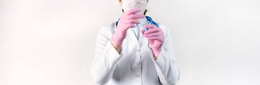 Beyaz önlüklü, tıbbi maskeli ve pembe steril eldivenli genç bir kadın doktorun elinde çocuklar ve yetişkinler için ampul aşı tutarken çekilmiş görüntüsü. Kavram: hastalıklar, tıbbi bakım, bilim, anestezi, ötenazi, diyabet.