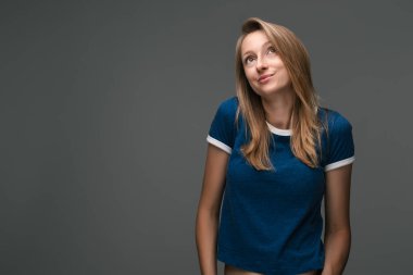 Sarışın, güzel bir kadının stüdyo fotoğrafı. Mavi tişört giyiyor, gizemli bakışlar atıyor. Yasadışı ya da gizlice bir şeyler yapmak istiyor.