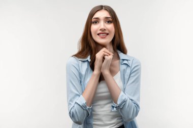 Karizmatik esmer kadın fotoğrafı, uzun düz saçlı, günlük kıyafetler giymiş, çenesinin yanında el ele tutuşan, nazikçe gülümseyen, hoş bir yüz ifadesi olan. İnsani duygular, yüz ifadesi kavramı.