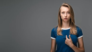 Stüdyodaki kızgın kadın kırıcı sözlerle ürküyor, kendini ön parmağıyla işaret ediyor şaşırarak ağzını açıyor, sorgulama ifadesi var, mavi tişört giyiyor. Boşluğu kopyala