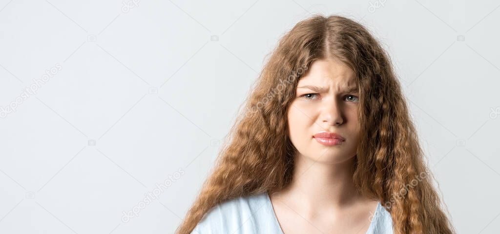 What wrong. Portrait of confused beautiful girl with curly long hair, smirks face, feels doubt while makes choice, dressed in casual t shirt. Isolated on white background.