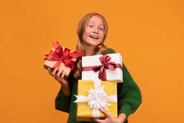 12-14 yaşlarında, elinde bir sürü hediye kutusu olan yeşil kazaklı çekici bir kız resmi. Stüdyo fotoğrafı, sarı arka plan, izole edilmiş. Yeni Yıl Kadınların Doğum Günü Tatil Konsepti