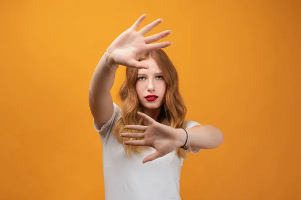 Image of serious woman 20s with long wavy blonde hair, wearing white t-shirt gestures actively hands at camera, stop gesture with hands. No way, stop doing