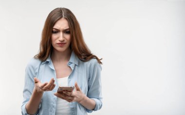 Uzun kestane rengi saçlı, sıradan kıyafetler giymiş, akıllı telefonu elinde tutan öfkeli genç bir kadın. Yeni uygulamayı nasıl kullanacağını bilmiyor. Stüdyo çekimleri beyaz arkaplan