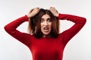 Uzun kestane rengi saçları olan, kırmızı süveter giyen, başını tutan genç ve stresli bir kadın resmi. Duygusal acizlik var. Sorunlar, sürpriz, korku, fobi konsepti. Stüdyo çekimi, beyaz arkaplan.