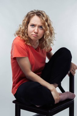 Düşüncelere dalmış, kıvırcık saçlı, sıradan tişörtler giymiş kameraya bakan güzel bir kadın resmi. İnsani duygular, yüz ifadesi kavramı. Stüdyo çekimi, beyaz arkaplan