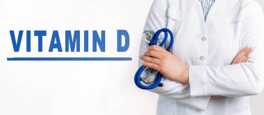 Beyaz arka planda Kelime VITAMIN D. Yakınlarda beyaz önlüklü ve steteskoplu bir doktor var. Tıbbi konsept