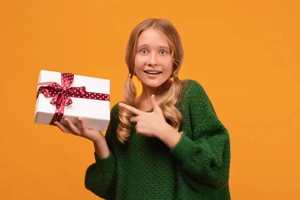 魅力的なブロンドの女の子のイメージ12 14歳暖かい緑のセーターで笑顔と赤い弓で現在のボックスを保持します スタジオ撮影 黄色の背景 新年の女性の誕生日の休日の概念 — ストック写真
