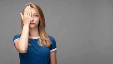 Yorgun, sarışın, yüzü örtülü, yorgun, iyi dinlenmesi gereken, mavi tişörtlü, gri arka planda izole genç bir kadın fotoğrafı. İnsani duygular, yüz ifadesi kavramı.