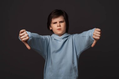 10-12 yaşlarında hoş bir çocuğun portresi, günlük giysiler giymiş, baş parmağını aşağı gösteriyor. Beceriksizlik kavramının aksine. Stüdyo fotoğrafı, gri arka plan. İnsani duygular, yüz ifadesi kavramı