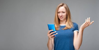 Sarı saçlı ve mavi tişörtlü rahatsız bir kız sorunlu bir yüz ifadesi takınıyor, akıllı telefon tutuyor, sorunun ne olduğunu anlayamıyor, mesajın garip bir anlamı var. Metnin için boşluk kopyala